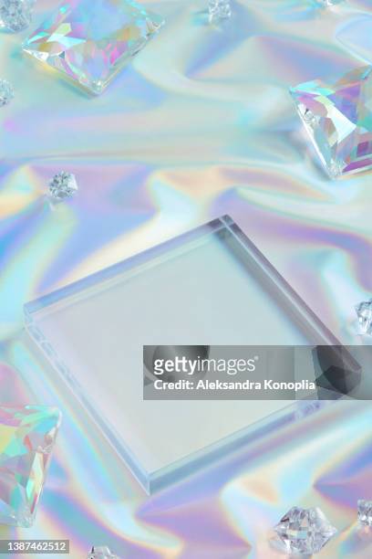 square glass podium and crystals on folded pastel neon reflective rainbow holographic textile background - blank packaging stock-fotos und bilder