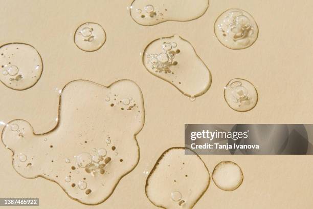transparent drops of serum on beige background. liquid hyaluronic acid gel. flat lay, top view. - etherische olie stockfoto's en -beelden