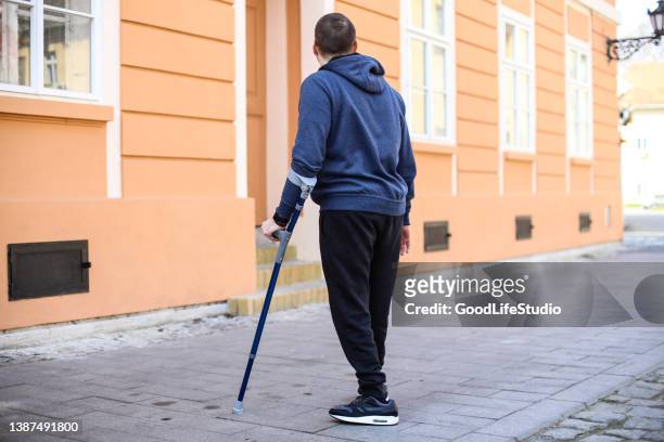 man walking with crutches on the street - crutches stockfoto's en -beelden
