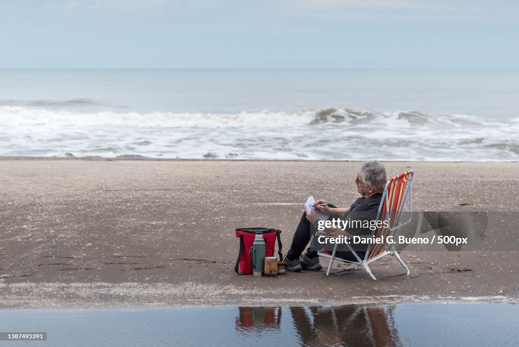 Adult man with gray hair and glasses sitting on a beach chair drawing