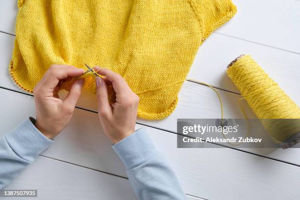 a young woman knits cotton and wool yarn knitting needles on a white wooden table background. next to him is a skein of thread. a girl in bright clothes holds yarn in her hands. the concept of handmade work, hobbies and creativity, freelance work. - knitting needles stock-fotos und bilder