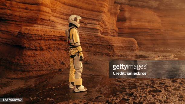 a walk on mars. female astronaut exploring rust mountains. climbing on rocks, looking at view - astronaut sitting stock pictures, royalty-free photos & images