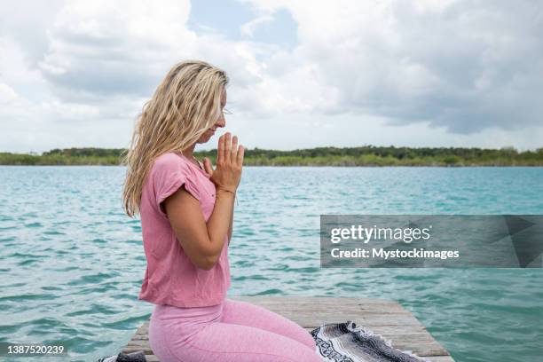 frau, die yoga auf holzpier an der lagune praktiziert, hände ans herz in namaste gebetspose - prayer pose greeting stock-fotos und bilder