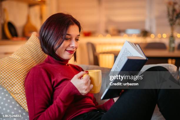 woman lying on sofa and reading book - escapism reading stock pictures, royalty-free photos & images