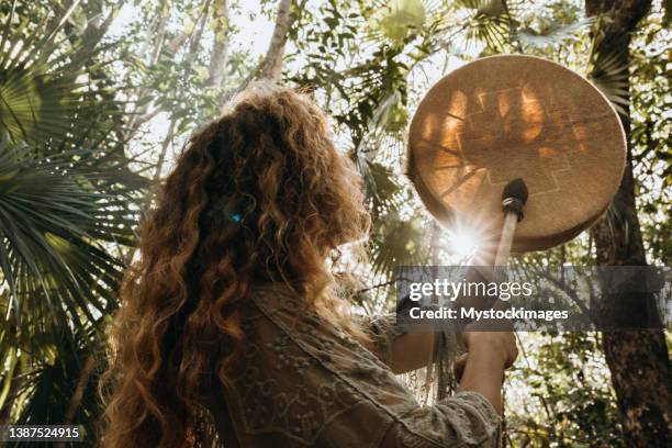 one multiracial woman practicing sound healing ceremony in the rainforest - drum stockfoto's en -beelden
