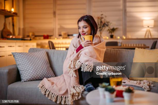 beautiful woman drinking hot tea wrapped in blanket - winter sofa stock pictures, royalty-free photos & images