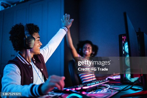 Friends doing a high five while playing on the computer at home Friends doing a high five while playing on the computer at home