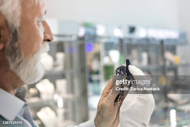 senior man in jewelry store selling luxury watches wiping wristwatch with a piece of cloth - rag time stockfoto's en -beelden