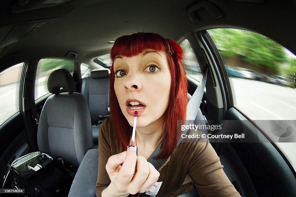 Young woman applying lip gloss while driving