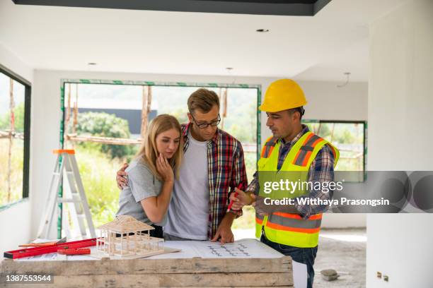 young couple looking blueprints of their home with handyman - architekt helm plan stock pictures, royalty-free photos & images