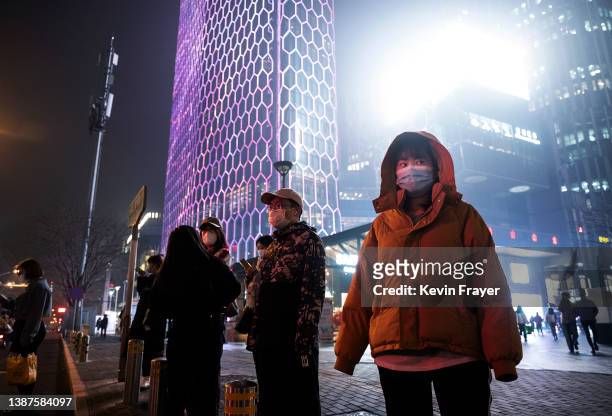 Pedestrians wait to cross a street in a shopping district on a polluted and foggy evening on March 24, 2022 in Beijing, China.