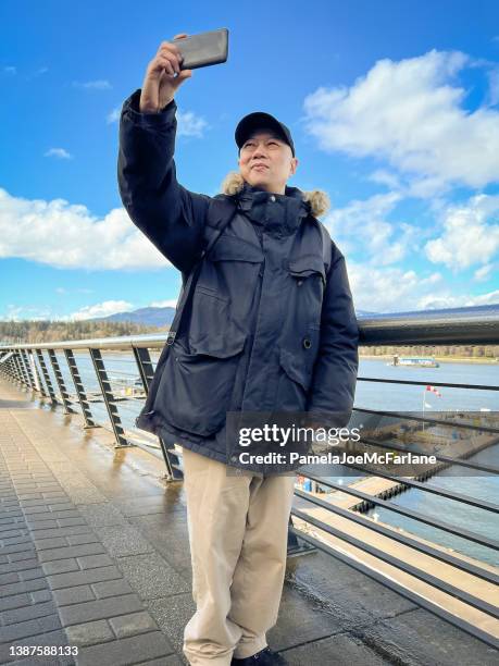 hombre maduro asiático gay tomándose una selfie con waterfront en el fondo - stanley park fotografías e imágenes de stock