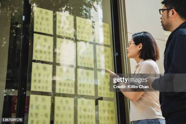 asian couple looking at advertisement from real estate office - real estate office stockfoto's en -beelden