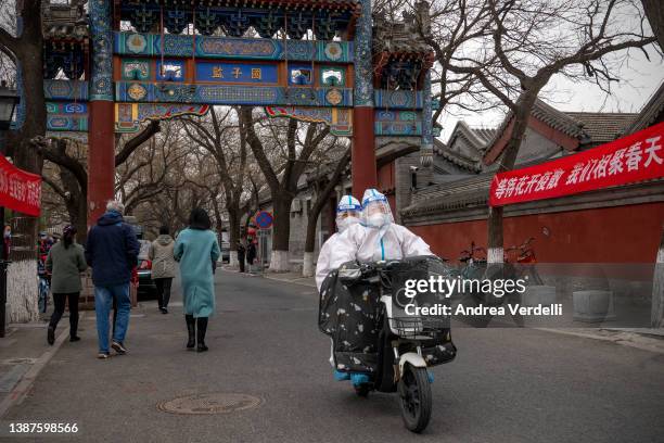 People decked in personal protective equipment ride an electric bike next to a mass testing site in a neighbourhood on March 25, 2022 in Beijing,...