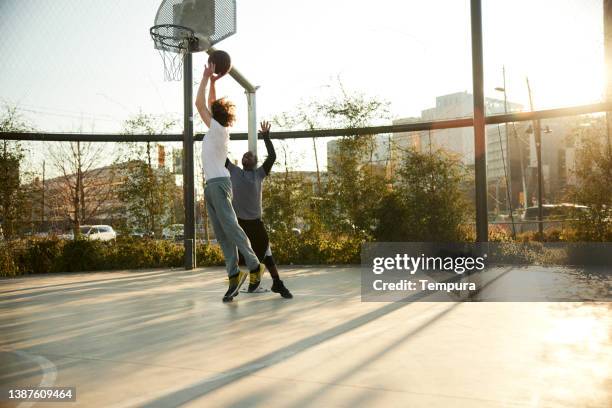 a one-on-one streetball action at a basketball court. - match basket stock pictures, royalty-free photos & images