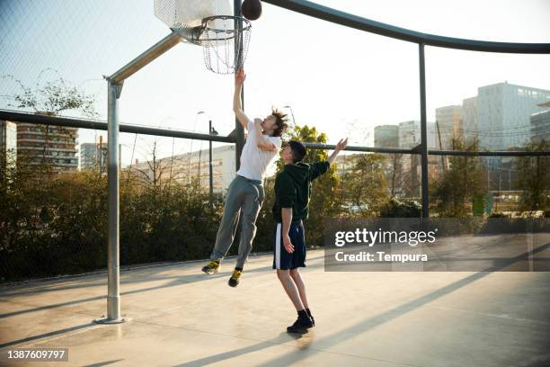 a young man attempts to score a shot with the opposition of a defender. - streetball stock pictures, royalty-free photos & images