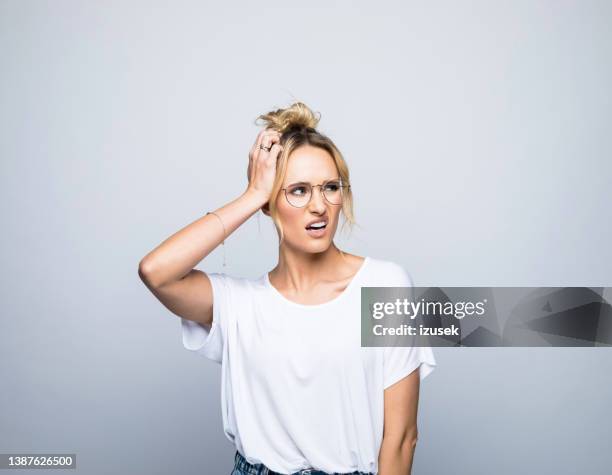 confused woman looking away while scratching head - unhappy woman blonde glasses stock pictures, royalty-free photos & images