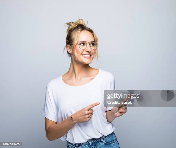 smiling blond woman pointing while looking away - finger bun stock pictures, royalty-free photos & images