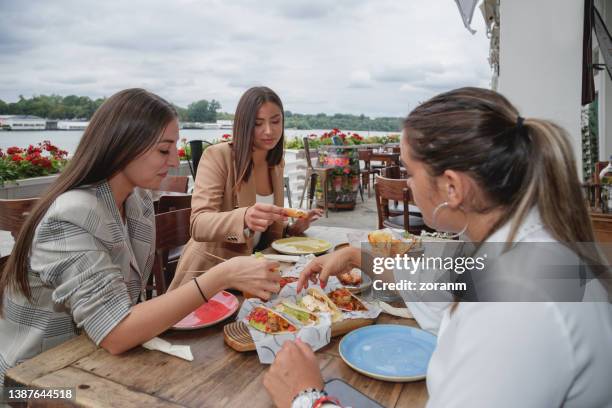 three young women eating tortilla chips and other mexican snacks in outdoor restaurant - tortilla stock pictures, royalty-free photos & images