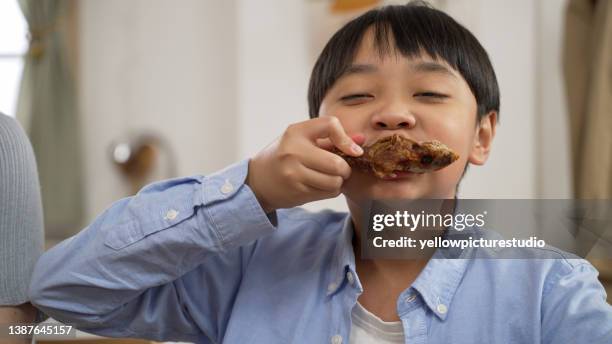 portrait of cute asian boy with yummy face enjoy eating roasted chicken drumstick, happy kid eating grilled chicken, healthy food for children concept - chicken fingers stockfoto's en -beelden