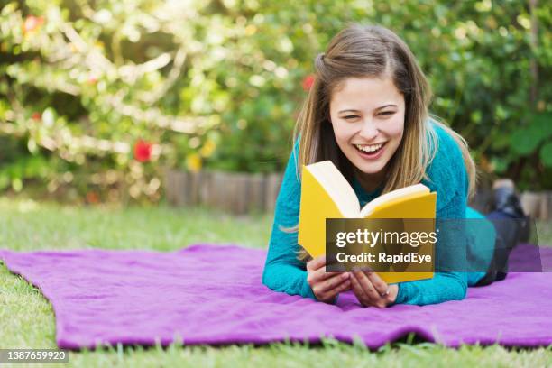 bella giovane donna che legge un libro mentre è sdraiata in un bellissimo giardino lussureggiante - libri gialli estate foto e immagini stock