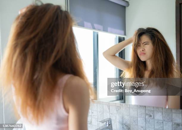 young worried asian woman while she saw her messy hair in the mirror after waking up in the morning. - frizzy 個照片及圖片檔