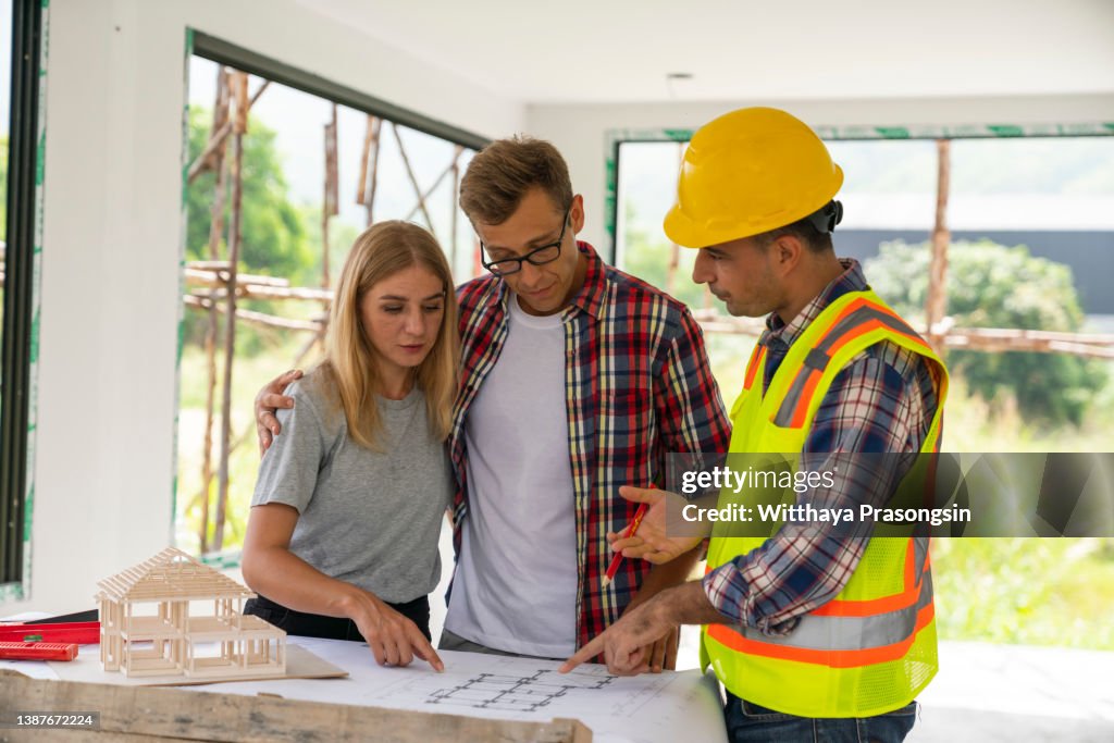Husband and wife consulting with a architect inside a home under construction.