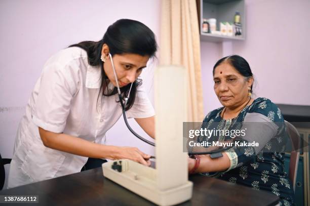 female doctor examining blood pressure of a senior woman patient - hypertensive stock pictures, royalty-free photos & images