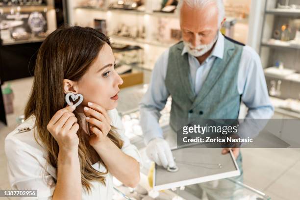 woman shopping for jewelry trying on earring - diamond necklace stock pictures, royalty-free photos & images