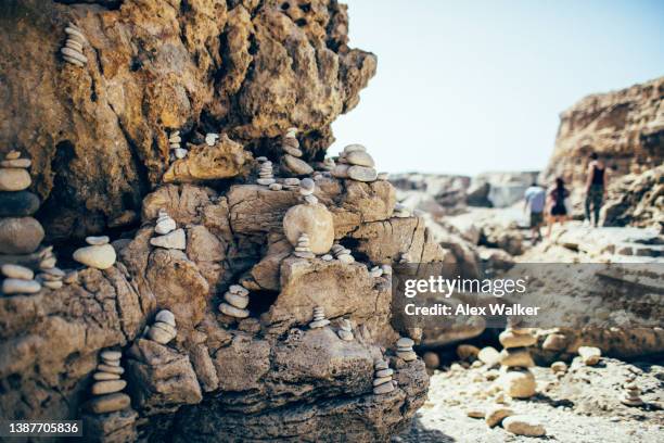 pebbles stacked in small balanced towers on the edge of limestone cliffs with tourists walking in the background. - azure window malta stock pictures, royalty-free photos & images