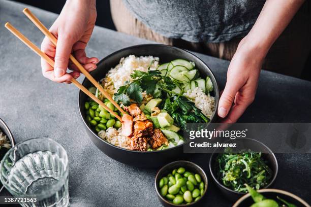 woman eating poke salad with chopsticks - tigela imagens e fotografias de stock