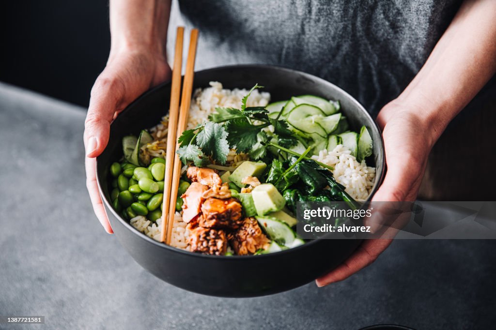 Frau hält eine Poke-Salatschüssel mit Essstäbchen in der Hand