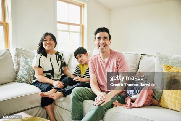 medium wide shot of smiling family watching television on couch in living room - familie hell weiss stock-fotos und bilder