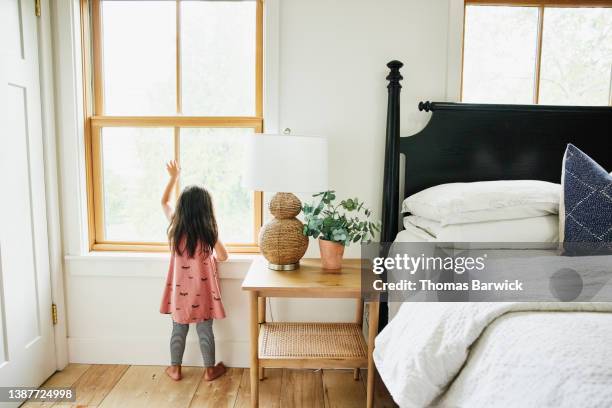 wide shot rear view of young girl waving out bedroom window - back cushion stock pictures, royalty-free photos & images