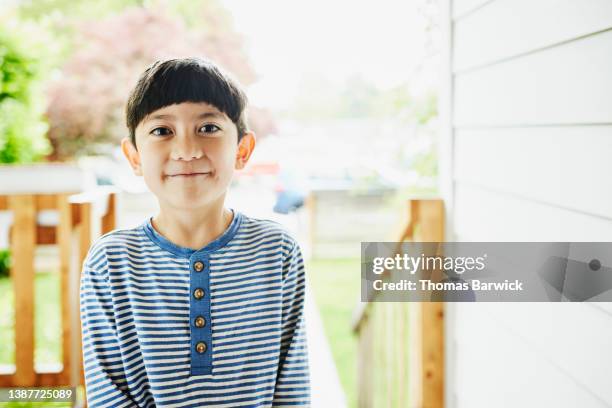 medium shot portrait of smiling boy standing on front porch of home - 8歳から9歳 ストックフォトと画像