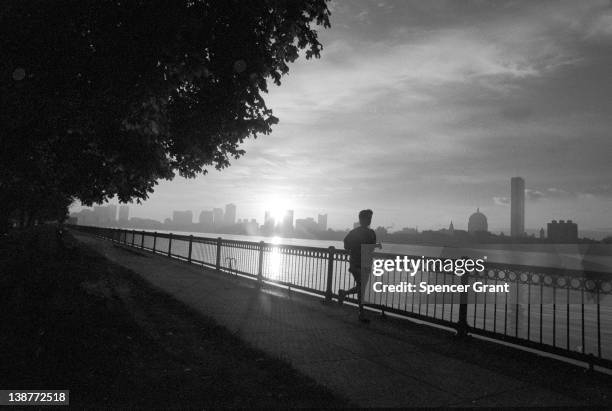 An early morning jogger runs along Memorial Drive, with the Charles River and city skyline in background, Cambridge, Massachusetts, 1972.