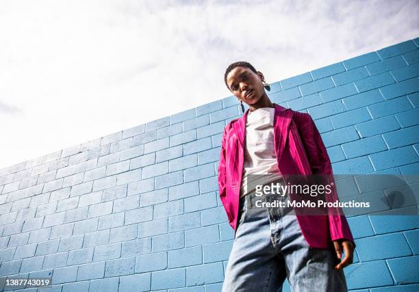 portrait of fashionable young woman in front of bright blue wall - pink blazer stock-fotos und bilder