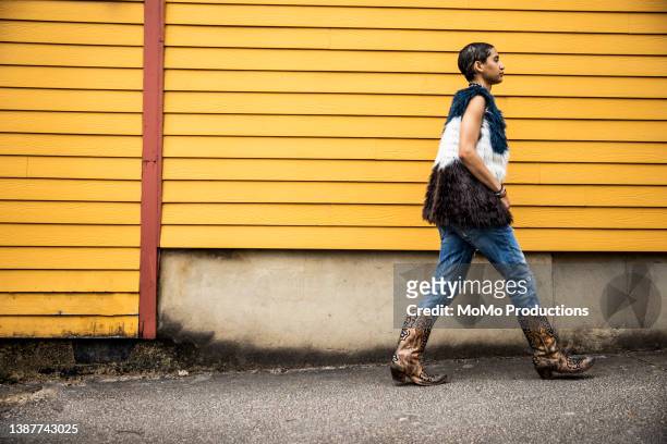 fashionable young woman walking in front of yellow urban home - cowboy boots stock pictures, royalty-free photos & images