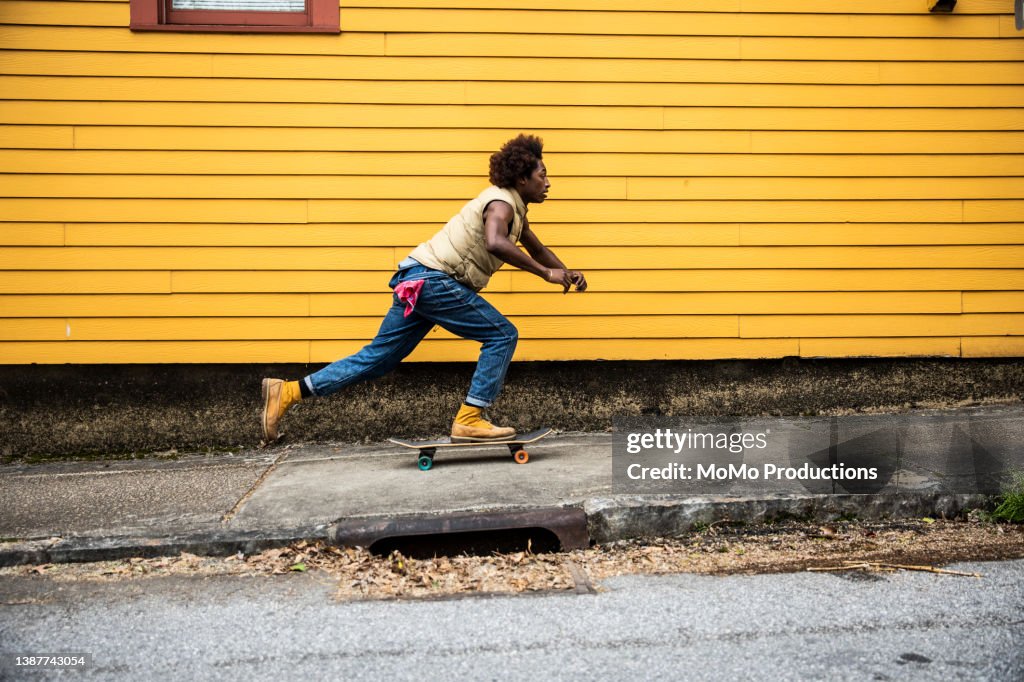 Fashionable young man skateboarding in front of yellow urban home
