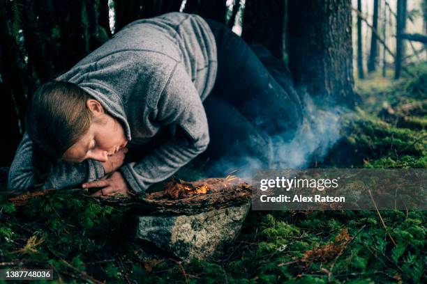 close up of a woman in a survival shelter trying to keep a small fire burning in a forest - makeshift shelter stock pictures, royalty-free photos & images