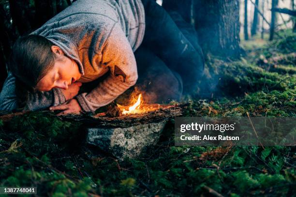 a woman tries to keep warm while laying beside a small fire in a wet rainforest - survival stock pictures, royalty-free photos & images