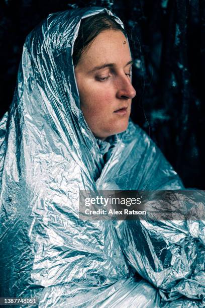 portrait of a woman shivering inside of a silver survival blanket in the wilderness - hyperthermia stockfoto's en -beelden