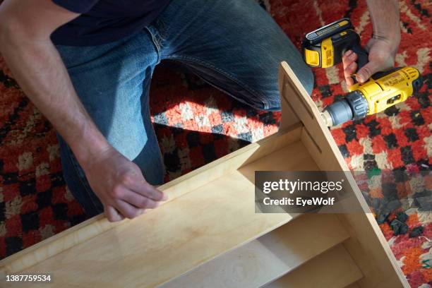 overhead shot of a man sitting on floor assembling a wooden bookshelf using a power drill - building shelves stock pictures, royalty-free photos & images