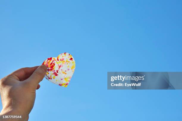 a hand holding a translucent cut out heart against a blue sky - opal card stock pictures, royalty-free photos & images