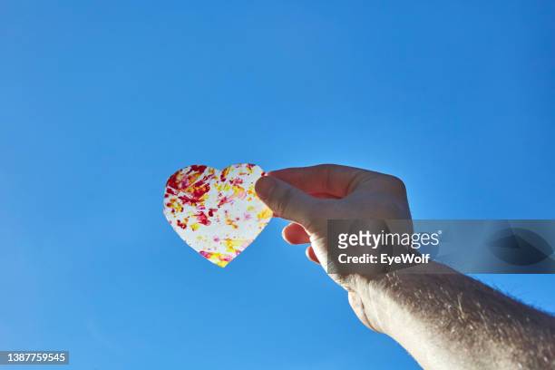 a hand holding a translucent cut out heart against a blue sky - opal card stock pictures, royalty-free photos & images