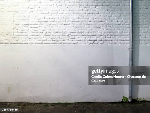 empty white brick and cement wall with pipe and cobbled street in brussels - wall night stock-fotos und bilder