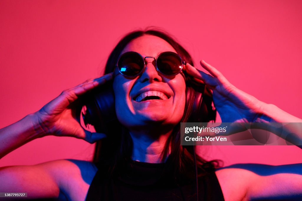 Pretty woman with sunglasses listening to music with headphones on neon background