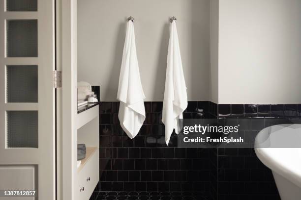 two new white towels hanging on the black-tiled bathroom wall - draped cloth stock pictures, royalty-free photos & images