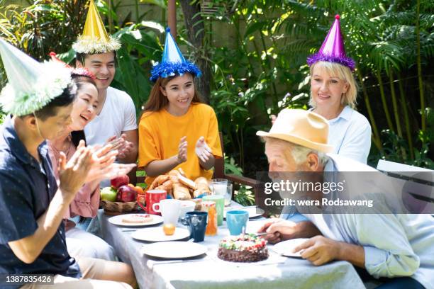 senior man blowing out birthday candles celebrate with family - parents children blow candles asians foto e immagini stock