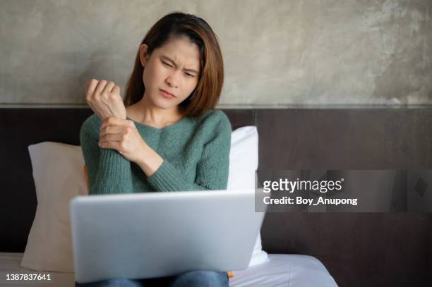 portrait of asian woman having wrist pain while working long period on laptop. office syndrome concept. - rheuma stock-fotos und bilder